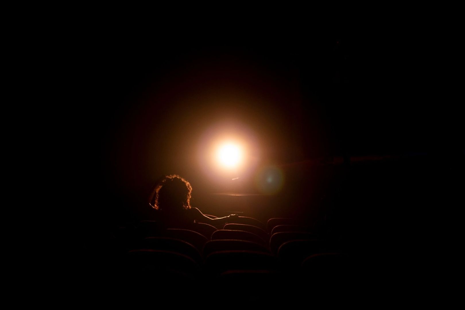 A lone cinema viewer faces a bright screen in a dark theater