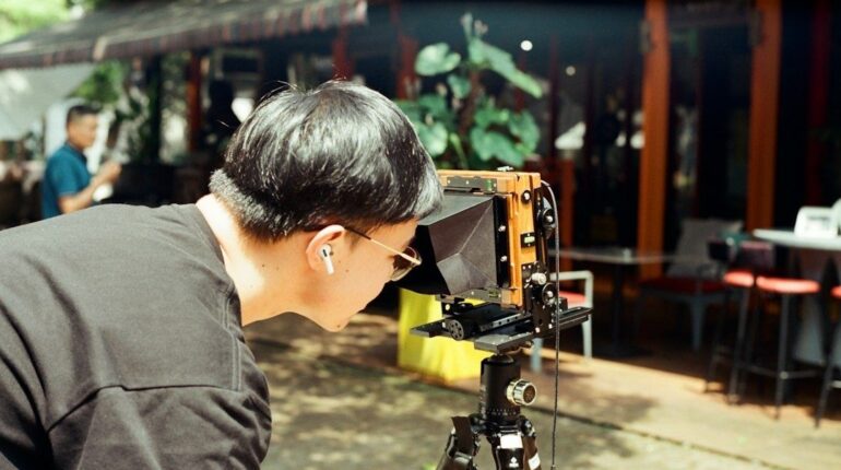 Person peers into a vintage camera on a tripod outdoors