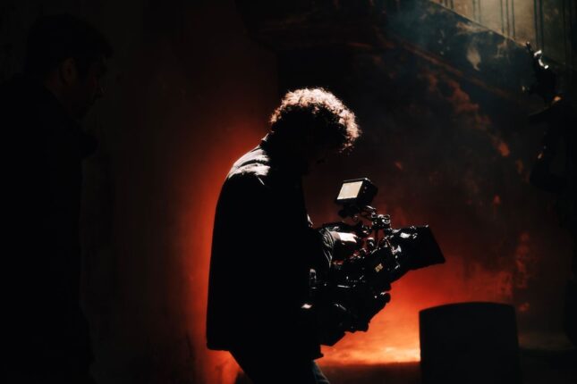 Cinematographer filming amid dramatic red-orange stage lighting