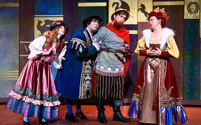 Four actors in ornate period costumes perform on a colorful stage